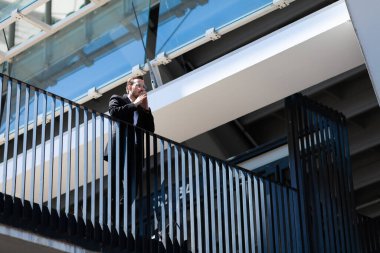 Businessman stands on balcony in thought, focused.