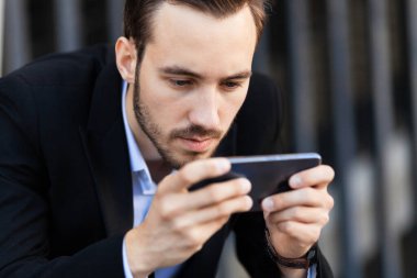 Genç işadamı telefona bakar (akıllı telefon), oynat. Bilgi bağımlılığı.