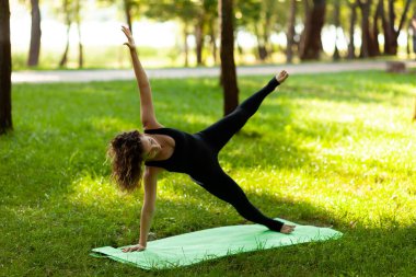 Kadın sabahları parkta temiz havada yoga yapıyor. Yan Plank duruşu.