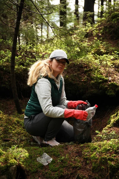 stock image Adult female volunteer cleans garbage and plastic that pollutes environment in forest.