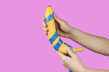 Measuring the size of a banana as a symbol of the male penis isolated on pink background. Big dick length. Strong erection and impotence problem.