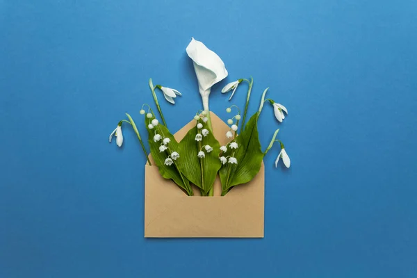 Spring flowers in a mail envelope on a blue background. Romantic birthday greetings, creative wedding invitation. Snowdrops, lilies of the valley and calla lilies.