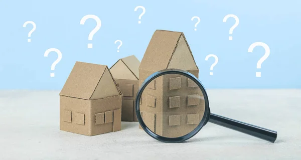 A question on a small house, a magnifying glass examines the building. Assistance in choosing and buying real estate.