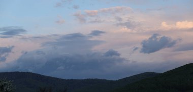 Dağların üzerinde bulutlu bir gökyüzünde gün batımı.