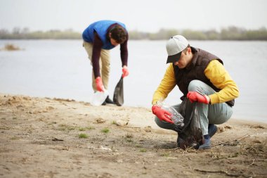 Adam gönüllü olarak sahildeki çöpleri kaldırıyor. Sahil çevre kirliliği, açık hava çöplüğü ve çöp..