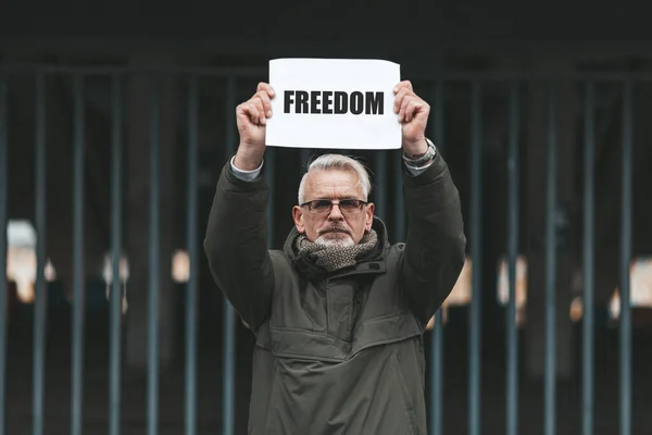 Protest for freedom against the background of the bars. An elderly man holds a poster with the words \
