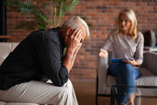 A session with a psychologist doctor, mental support. A mature man sits holding his head. Psychological problems in an elderly people.
