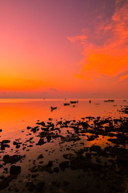 Sahilde gün doğumu ve demirli balıkçı teknelerinin siluetleri