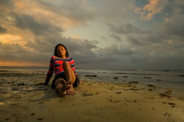 Gün batımında deniz kenarında oturan kadın.