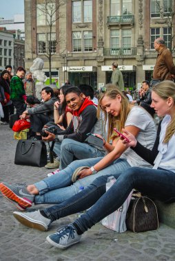 Amsterdam, Hollanda - 1 Nisan 2014: Cep telefonlarıyla bir şehir parkında oturan bir grup insan