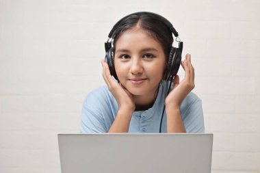 Bir kız dizüstü bilgisayarda müzik dinlemek için kulaklık takıyor.