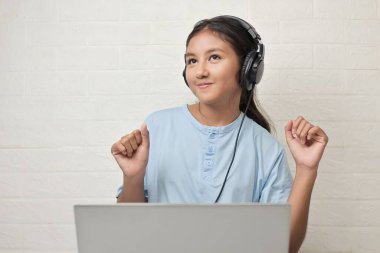 Bir kız dizüstü bilgisayarda müzik dinlemek için kulaklık takıyor.