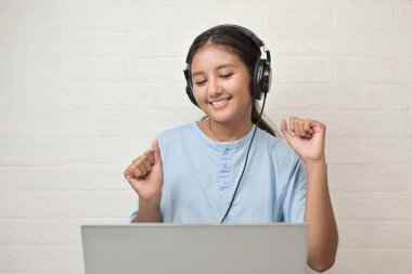 Bir kız dizüstü bilgisayarda müzik dinlemek için kulaklık takıyor.