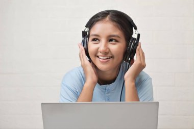 Bir kız dizüstü bilgisayarda müzik dinlemek için kulaklık takıyor.