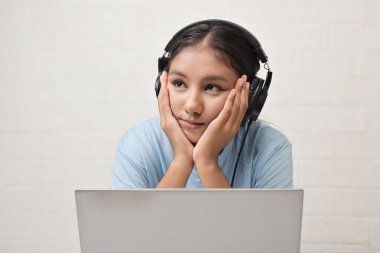 Bir kız dizüstü bilgisayarda müzik dinlemek için kulaklık takıyor.