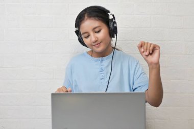 Bir kız dizüstü bilgisayarda müzik dinlemek için kulaklık takıyor.