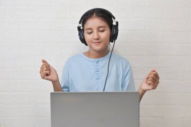 Bir kız dizüstü bilgisayarda müzik dinlemek için kulaklık takıyor.