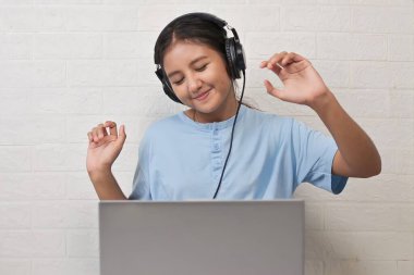 Bir kız dizüstü bilgisayarda müzik dinlemek için kulaklık takıyor.