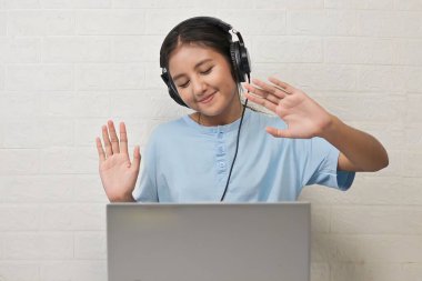 Bir kız dizüstü bilgisayarda müzik dinlemek için kulaklık takıyor.