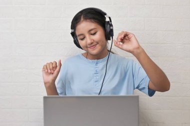 Bir kız dizüstü bilgisayarda müzik dinlemek için kulaklık takıyor.