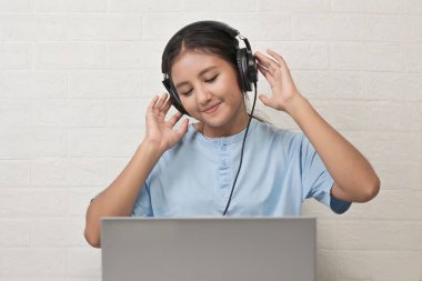 Bir kız dizüstü bilgisayarda müzik dinlemek için kulaklık takıyor.