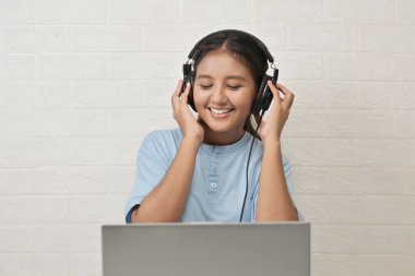 Bir kız dizüstü bilgisayarda müzik dinlemek için kulaklık takıyor.