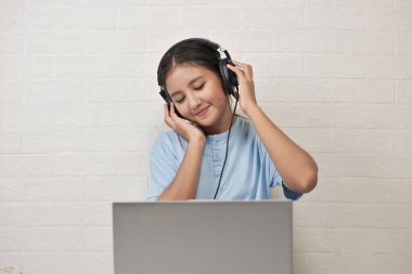 Bir kız dizüstü bilgisayarda müzik dinlemek için kulaklık takıyor.