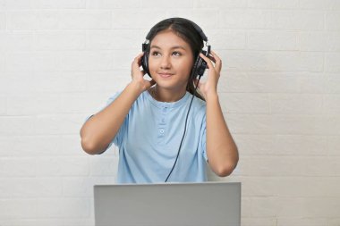 Bir kız dizüstü bilgisayarda müzik dinlemek için kulaklık takıyor.