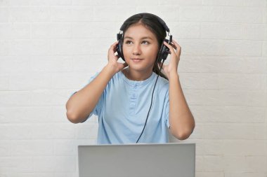 Bir kız dizüstü bilgisayarda müzik dinlemek için kulaklık takıyor.