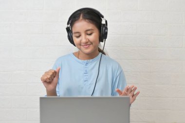 Bir kız dizüstü bilgisayarda müzik dinlemek için kulaklık takıyor.