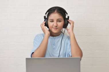 Bir kız dizüstü bilgisayarda müzik dinlemek için kulaklık takıyor.