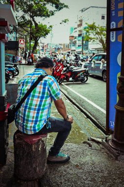 Ambon, Endonezya - 4 Nisan 2024: Bir adam şehir yolunun kenarında oturuyor