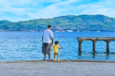 Ambon, Endonezya - 5 Nisan 2024: Bir adam ve çocuğu sahilde duruyor