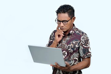 Batik gömlek giyen ve dizüstü bilgisayar üzerinde çalışan Endonezyalı bir adam.
