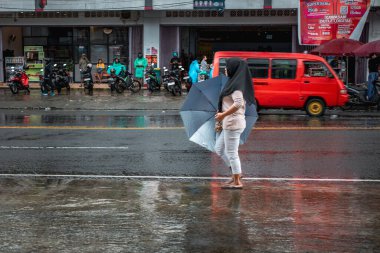 Ambon, Endonezya - 5 Haziran 2024: İnsanlar yağmurdan dolayı şemsiye taşırken yürüyorlar