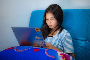 Asyalı bir kız yatağında dizüstü bilgisayarla çalışıyor.