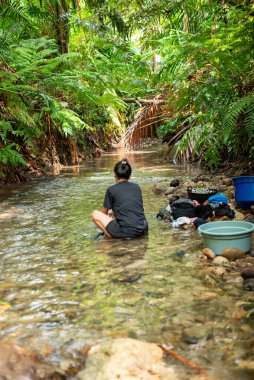 Endonezya - 15 Haziran 2024: Bir kadın ormanda küçük bir nehirde çamaşır yıkıyor