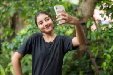 Parkta akıllı telefonla oynayan Asyalı kadın.