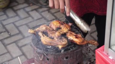 Asyalı sokak satıcısı Ayam Bakar 'ı (Izgara Tavuk) dumanlı ızgarada pişiriyor. Ayam bakar, kömürle kızartılmış tavuktan oluşan Endonezya ve Malezya yemeğidir..