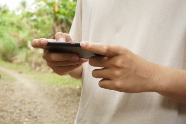 Endonezyalı genç bir adamın dokunmatik ekranlı akıllı telefondaki uygulamaları kullanması - Teknoloji, online alışveriş, mobil uygulamalar, mesajlaşma, telefon bağımlılığı için kavram.
