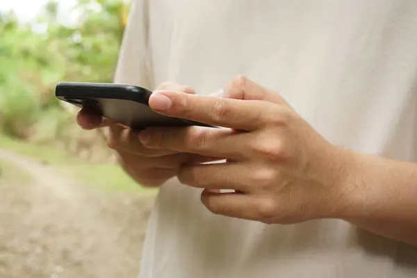 Endonezyalı genç bir adamın dokunmatik ekranlı akıllı telefondaki uygulamaları kullanması - Teknoloji, online alışveriş, mobil uygulamalar, mesajlaşma, telefon bağımlılığı için kavram.