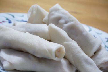 Tabakta çiğ börek (lumpia) yığını var. Ahşap masalarda donmuş yiyecekler..