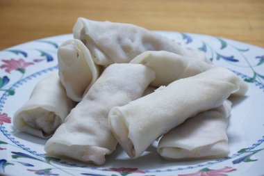 Tabakta çiğ börek (lumpia) yığını var. Ahşap masalarda donmuş yiyecekler..