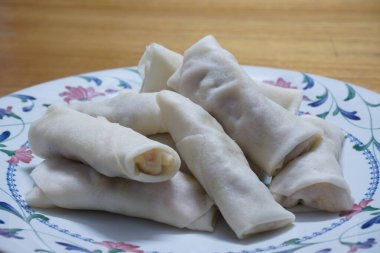 Tabakta çiğ börek (lumpia) yığını var. Ahşap masalarda donmuş yiyecekler..