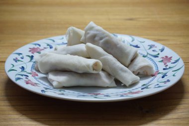 Tabakta çiğ börek (lumpia) yığını var. Ahşap masalarda donmuş yiyecekler..