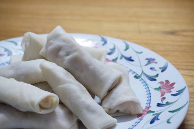 Tabakta çiğ börek (lumpia) yığını var. Ahşap masalarda donmuş yiyecekler..