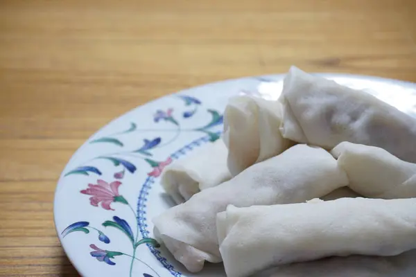 Tabakta çiğ börek (lumpia) yığını var. Ahşap masalarda donmuş yiyecekler..