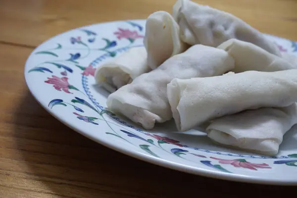 Tabakta çiğ börek (lumpia) yığını var. Ahşap masalarda donmuş yiyecekler..