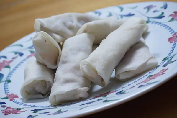 Tabakta çiğ börek (lumpia) yığını var. Ahşap masalarda donmuş yiyecekler..