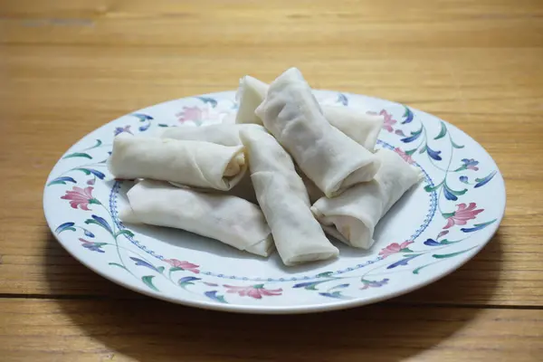 Tabakta çiğ börek (lumpia) yığını var. Ahşap masalarda donmuş yiyecekler..